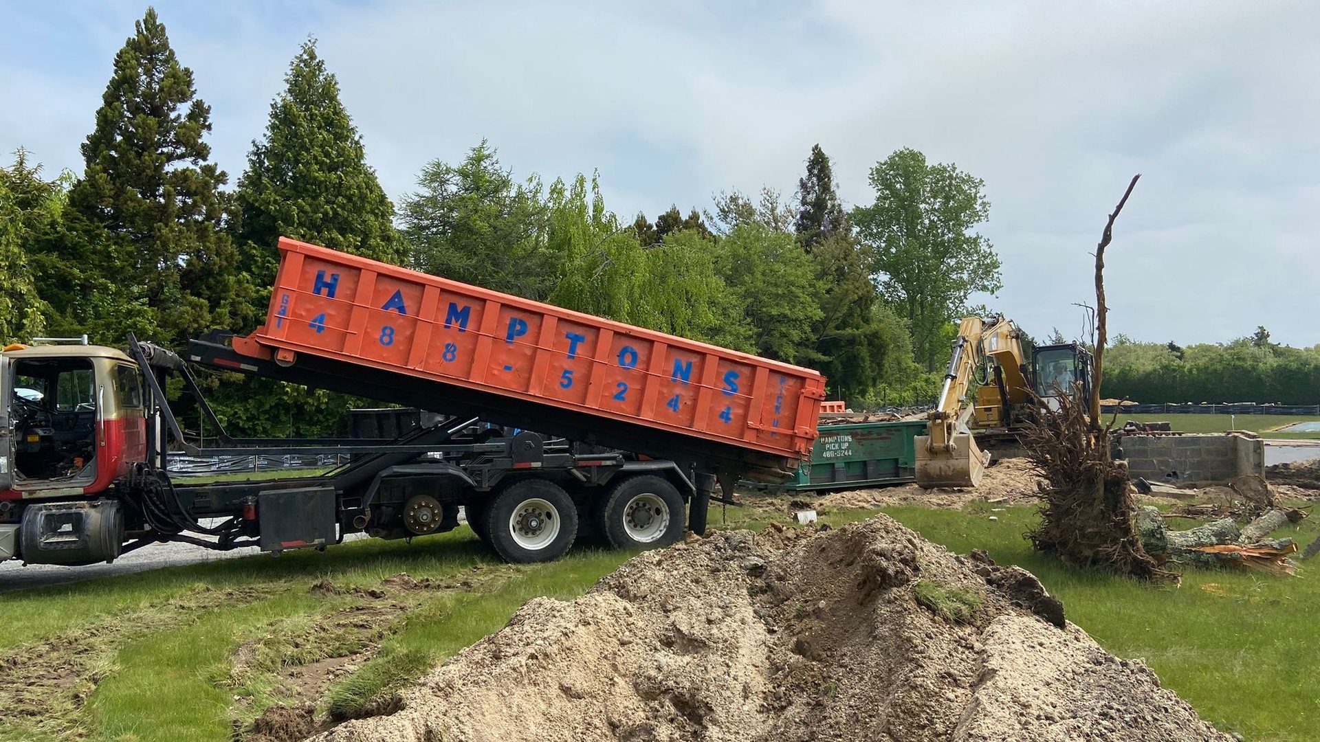 A Hamptons Pick Up truck emptying an orange roll-off dumpster at an East End construction site